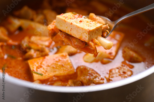 Kimchi soup with tofu and pork cooking in pot and eating by spoon, Korean food
