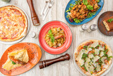 Italian food dishes viewed from above. Pasta di mare, rucola pizza, risotto di mare, tiramisu, guanciale pizza, forks, pepper shakers and salt shakers