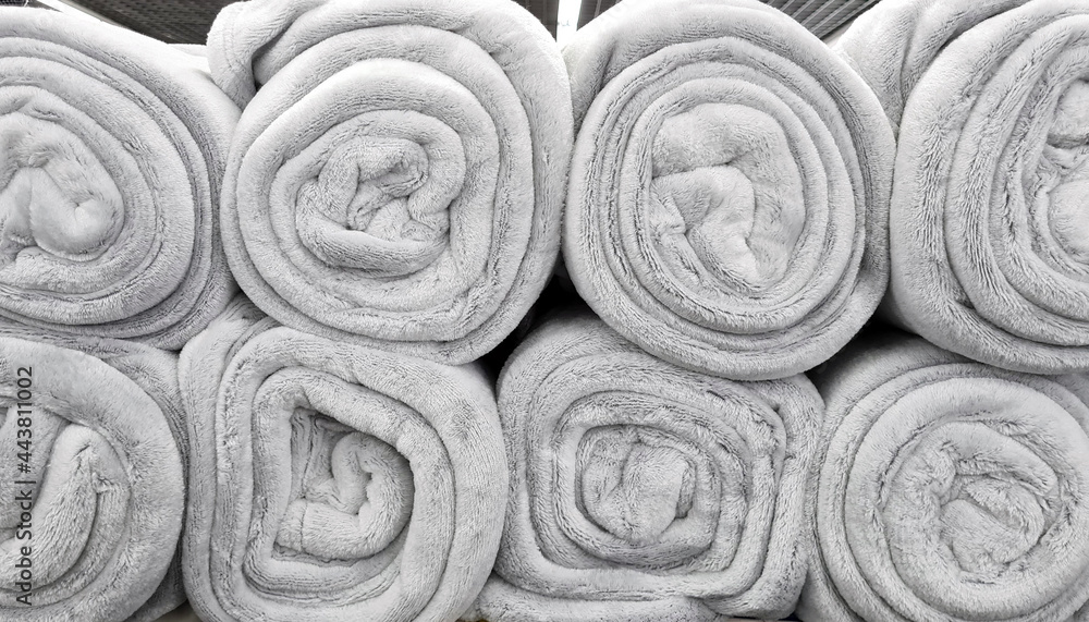 Rolled gray blankets in a store for sale. Soft fluffy beige plaids sells in shop shelf. Rolled gray blankets in a store for sale. Soft fluffy beige plaids sells in shop shelf.