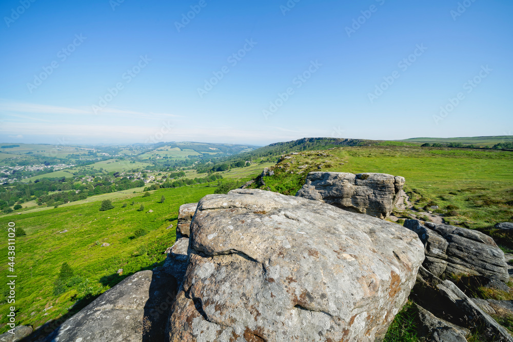 Along the top of Baslow Edge, over weathered gritstone boulders to a distant, hazy Curbar Edge