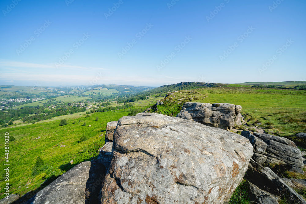 Fototapeta premium Along the top of Baslow Edge, over weathered gritstone boulders to a distant, hazy Curbar Edge