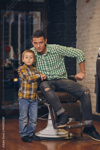 Young handsome father and his little stylish son at barbershop waiting for barber
