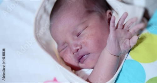 Asian newborn baby girl makes arm and hand movements extreme close-up shot. Adorable 0–6-month-old infant with closed eyes. Neonatal care of first days in life concept. photo