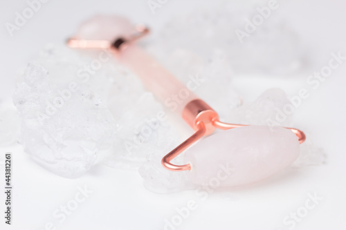 Concept of cooling skin care for summer and lymphatic drainage massage. Closeup of a rose quartz roller surrounded by ice.