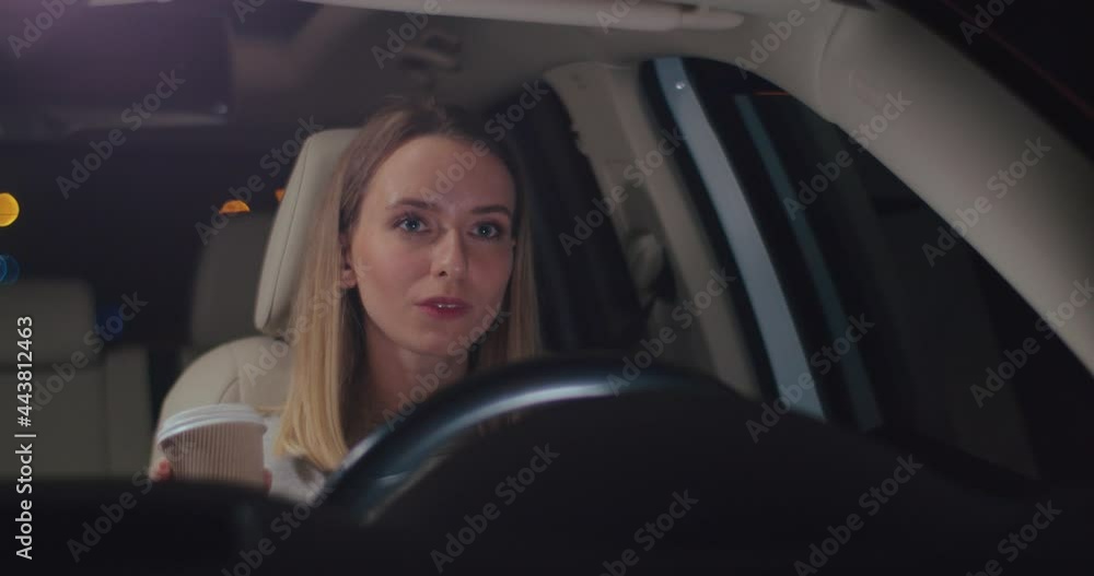 Dont sleep. Happy caucasian woman drinking her hot coffee and looking at the road while driving the car at the dark night. Energetic concept Dont sleep. Happy caucasian woman drinking her hot coffee and looking at the road while driving the car at the dark night. Energetic concept