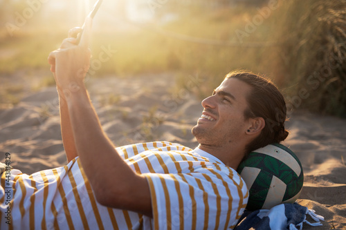 Handsome guy chilling at the beach. Young man using the phone while resting on the sandy beach photo