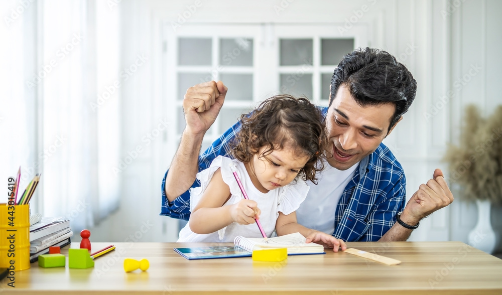 Portrait of young father teaching his cute little daughters' study. Excited smiling small child girl enjoying learning with pleasant dad at home. Children education, home schooling concept