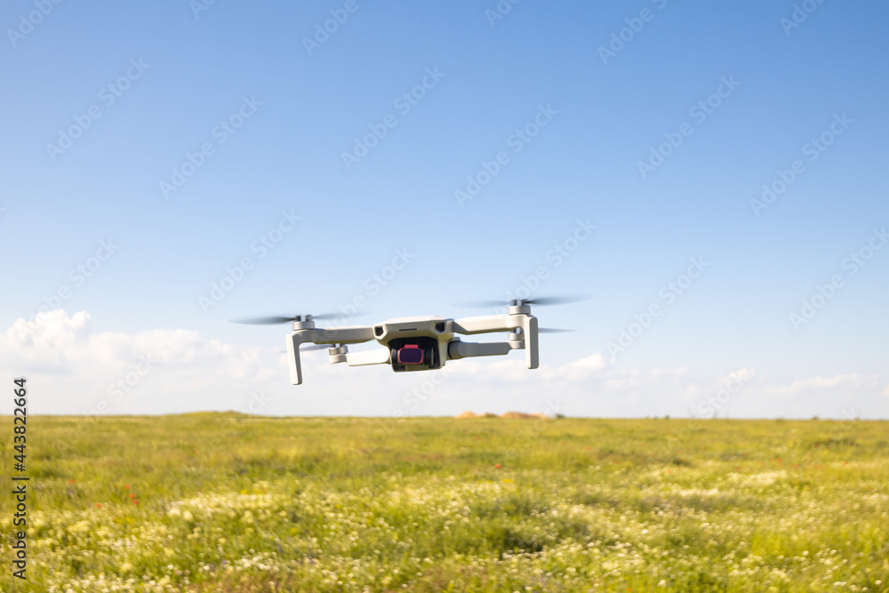Flying white drone quadcopter with camera in green field Flying white drone quadcopter with camera in green field