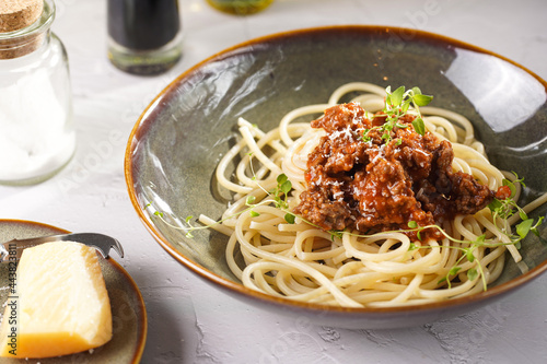 Italian spaghetti with bolognese tomato sauce and fresh thyme in dark green bowl on white concrete surface, with olive oil and balsamic vinegar in the back