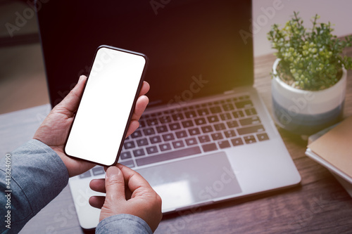 mockup image smartphone blank screen for hand typing text,using laptop contact business searching information in workplace on desk at office.design creative work space vintage tone concept.