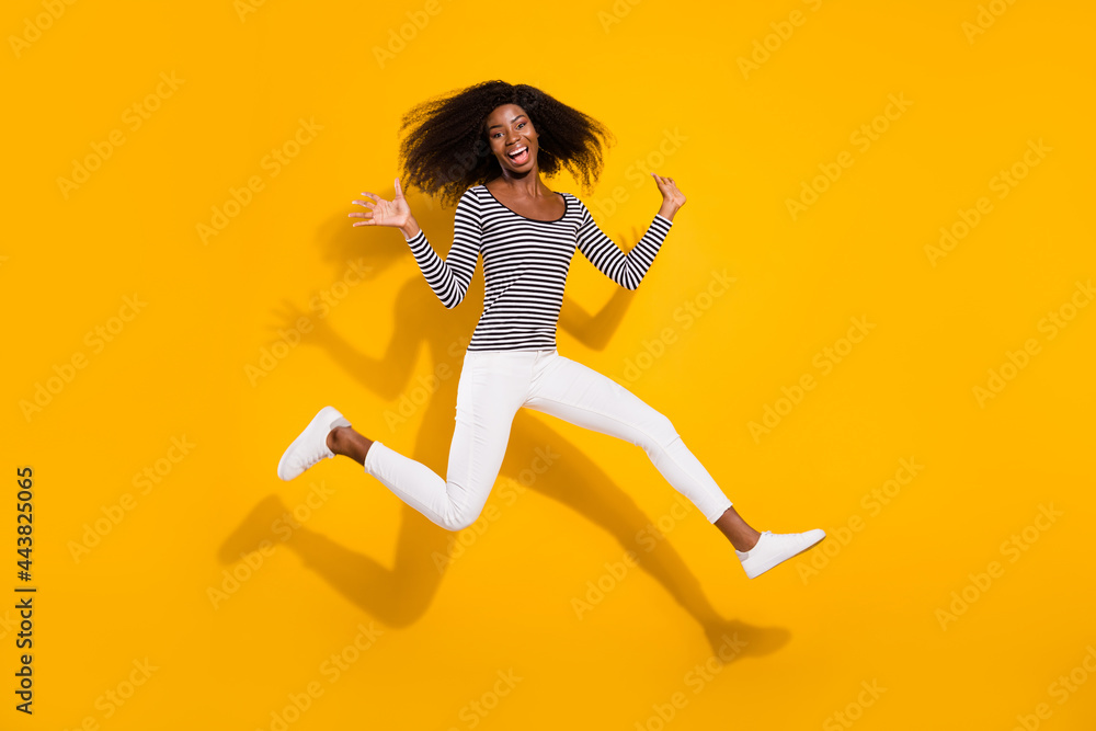 Full length body size photo woman in white pants jumping up laughing isolated vibrant yellow color background Full length body size photo woman in white pants jumping up laughing isolated vibrant yellow color background