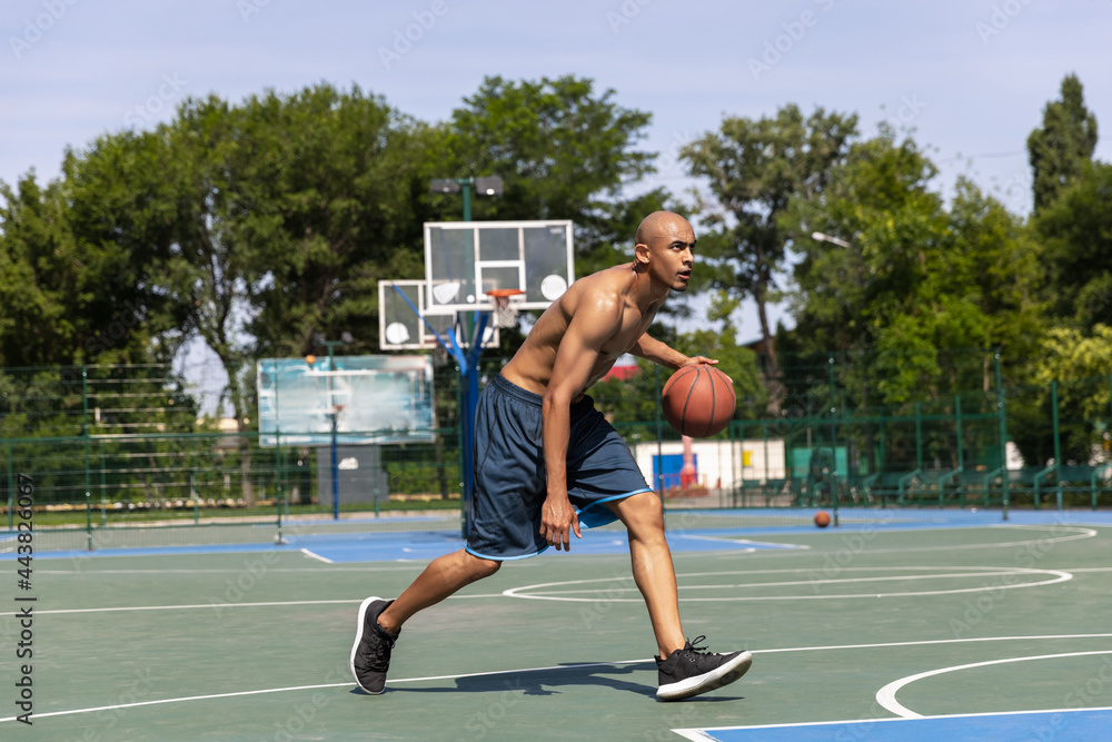 Obraz premium Strong muscular african-american male basketball player training at street public stadium, sport court or palyground outdoors. Summer sport games.