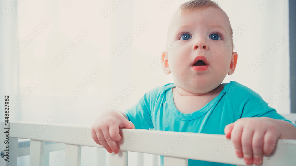 surprised baby boy standing in baby crib and looking up surprised baby boy standing in baby crib and looking up