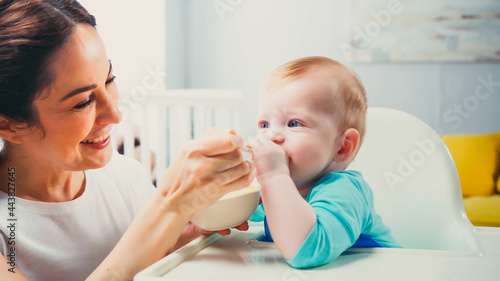 cheerful mother smiling while feeding infant son
