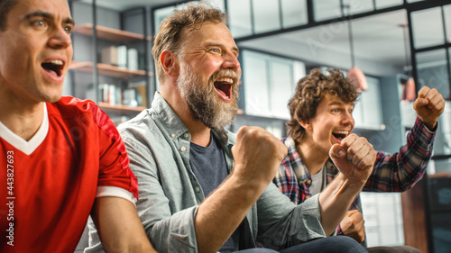 Obraz na plátně At Home Three Joyful Soccer Fans Sitting on a Couch Watch Game on TV, Celebrate Victory when Sports Team Wins Championship