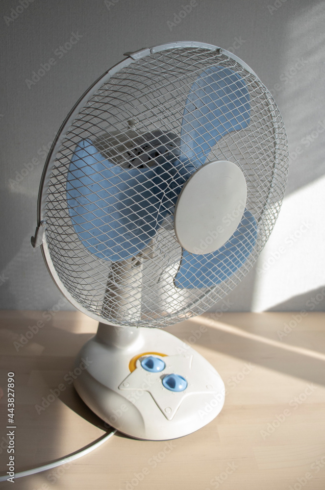 a white fan stands on the window in the apartment during the day. Cooling  system, room air conditioning, hot summer 2021. Window fan, shortage Stock  Photo | Adobe Stock