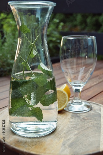 Glass, lemon and bottle filled with water and lemon balm, standing on a round wooden tray on wooden table outside. 