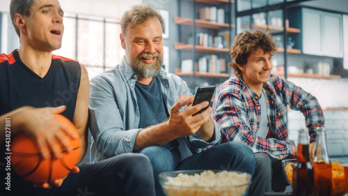 Photography At Home Three Fans Sitting on Couch Watch Basketball Game on TV, Use Smartphone App for Checking Score, Bet, Statistics, Celebrate when Team Wins Championship