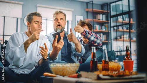 Photography Home: Three Ice Hockey Fans Sitting on a Couch Watch Game on TV, Use Smartphone App to Online Bet, Celebrate Victory when Sports Team Wins