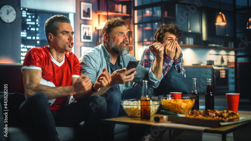 Fotografija Night at Home: Three Soccer Fans Sitting on a Couch Watch Game on TV, Use Smartphone App to Online Bet, Celebrate Victory when Sports Team Wins