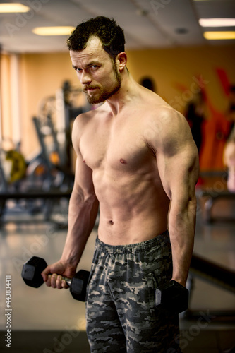 A young man of athletic physique is engaged with dumbbells in the gym.