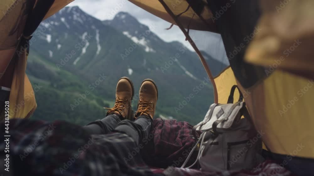 Women's legs in yellow hiking boots lie in a yellow tent. The traveler is resting, admiring the mountains after climbing. Yellow boots against the background of big mountains. Rest in the camp. Women's legs in yellow hiking boots lie in a yellow tent. The traveler is resting, admiring the mountains after climbing. Yellow boots against the background of big mountains. Rest in the camp.