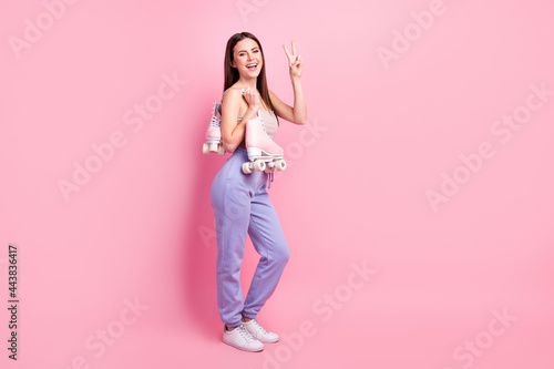 Full length body size view of attractive cheerful girl showing v-sign carrying rollers isolated over pink pastel color background