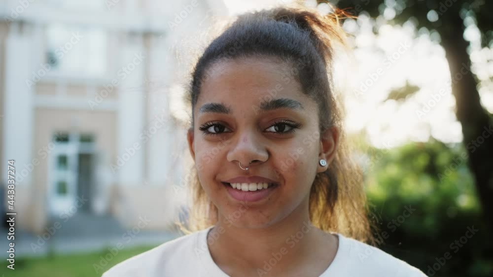 Portrait of funky african american girl student smiling happily, looking at camera on urban background.