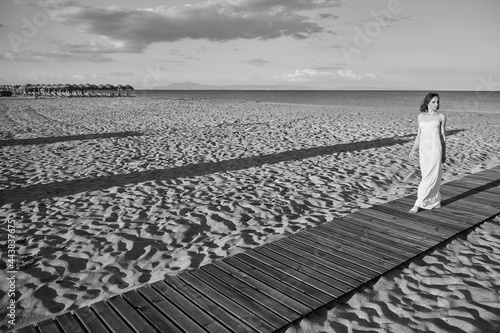black and white photo of a girl in a white dress on a background of the sea walking on the sand