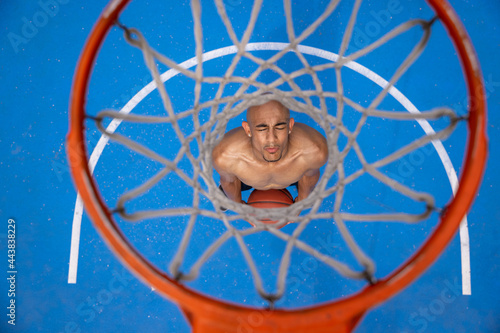 Top view through basketball hoop. Young man basketball player at street public stadium, sport court or palyground outdoors. Concept of healthy active lifestyle, motion, hobby. photo