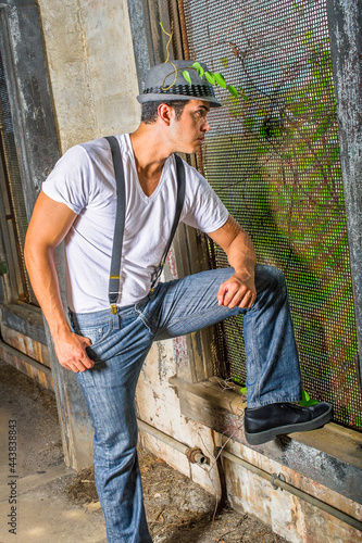 a young handsome guy is standing inside a abandoned house, looking through a screen window. .