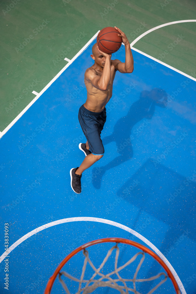 Top view of young man, male basketball player playing basketball at street public stadium, sport court or palyground outdoors. Summer sport games.