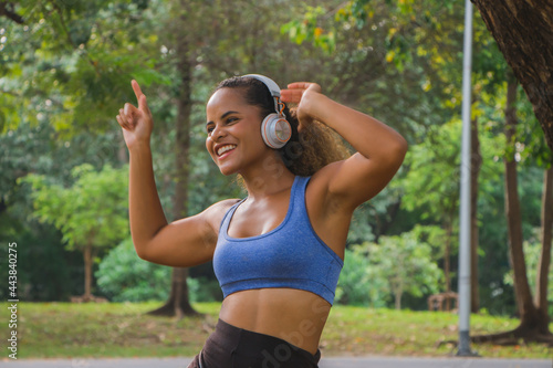 African american woman listening to music with headphones and smiling in park.