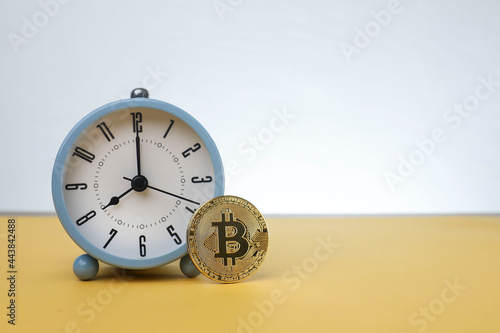 A Bitcoin standing against an alarm clock isolated on the yellow background 