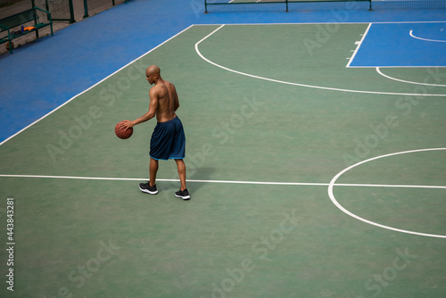 Top view of young man, male basketball player playing basketball at street public stadium, sport court or palyground outdoors. Summer sport games.
