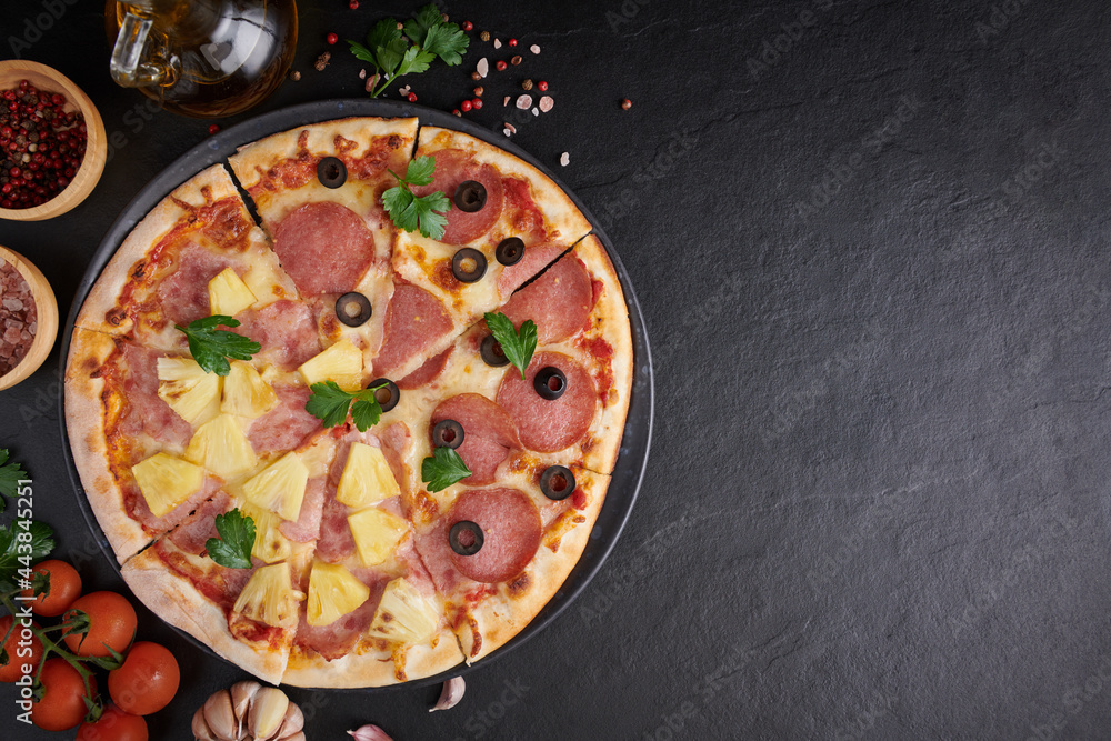 Italian pizza and pizza cooking ingredients on black concrete background. Tomatoes on vine, mozzarella, black olives, herbs and spices. Mixture pizza Italian food. Copy Space. Top view.