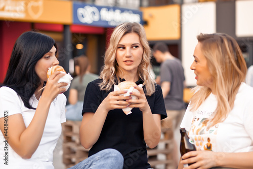 Pretty young women eating hamburger outdoor on the street