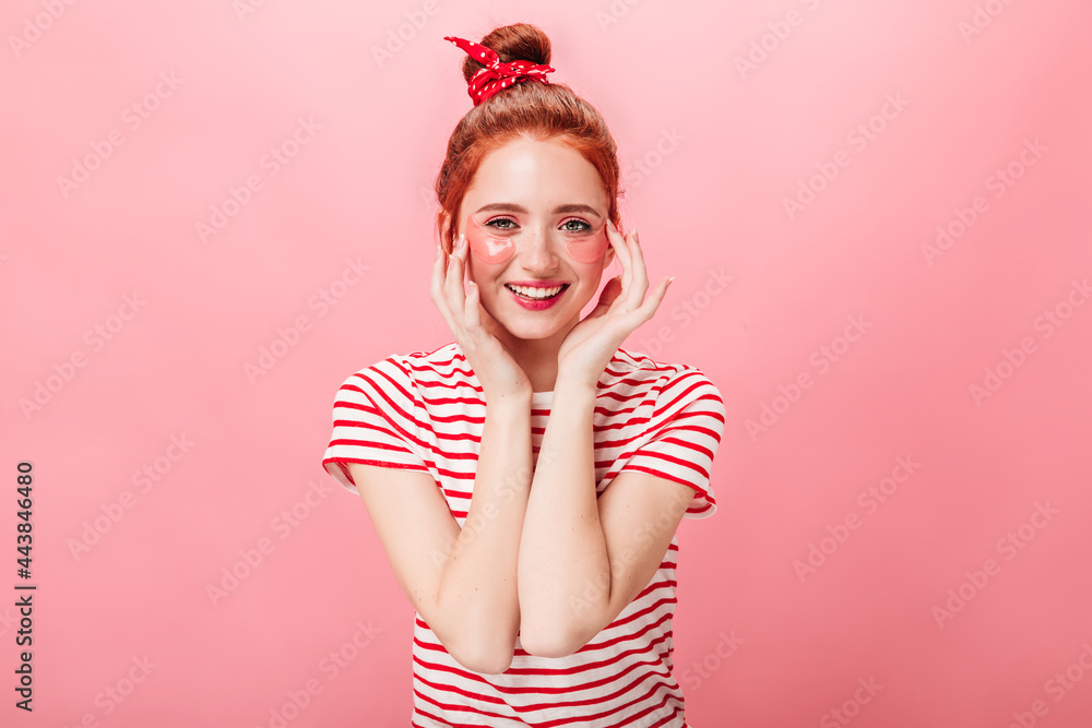 Front view of stylish young woman with eye patches looking at camera. Studio shot of ginger girl doing skincare treatment isolated on pink background. Front view of stylish young woman with eye patches looking at camera. Studio shot of ginger girl doing skincare treatment isolated on pink background.