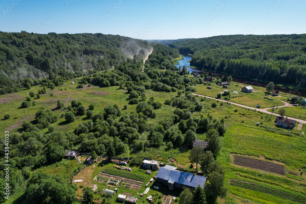aerial view river flowing village on the river bank in the middle of the forest dust on a dirt road from a passing car