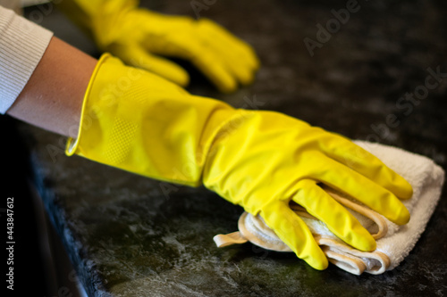  Woman housewife cleans the housein yellow gloves wipes the dust off the kitchen table against the plate