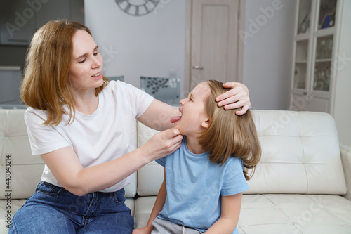 the little girl complains of a sore throat and her mother examines it. 