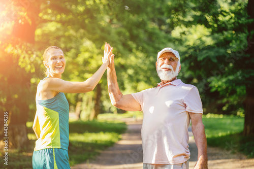 Fitness, rehab, sport, gesture, people and relation concept. Happy elderly man and overjoyed young nurse or daughter woman giving high five outdoors at summer park. Sun glare.