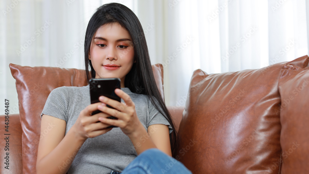 Young smart and active asian female sitting on sofa in living room, using smartphone with wireless earphone and happy smiling face Young smart and active asian female sitting on sofa in living room, using smartphone with wireless earphone and happy smiling face