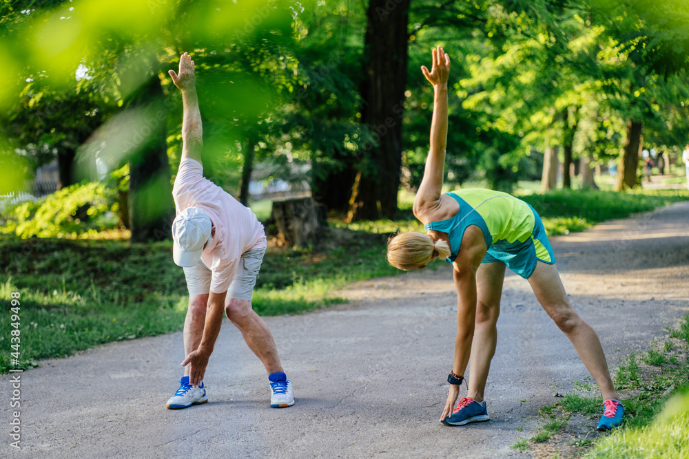 Obraz premium Fitness, sport, exercising, training and people concept. close up of senior man and young blond woman in activewear stretching on city park, outdoor.