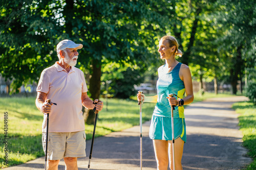 A blond sporty daughter take care of her father 80 year. Senior man very happy when go to walk at summer park, using trekking sticks. Concept care nurse with old people. © Iryna