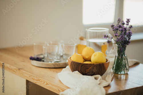 Wooden bowl with fresh lemons, emty glasses on a tray standing on a kitchen table.