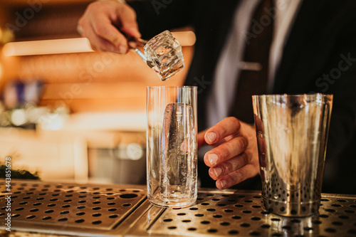 Close up shot of a bartender putting ice and preparing a cocktail. Concept of hospitality and bartending. Horizontal image, focus on barman’s hands
