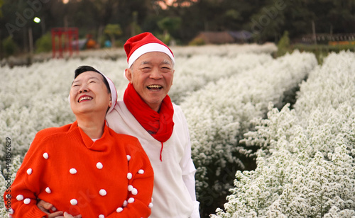 Asian senior eldery couple hugging sweater celecrate Christmas and New Year holiday morning in beautiful flowers garden photo