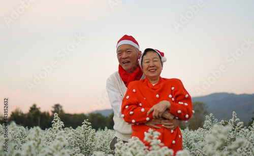 Asian senior eldery couple hugging sweater celecrate Christmas and New Year holiday morning in beautiful flowers garden photo