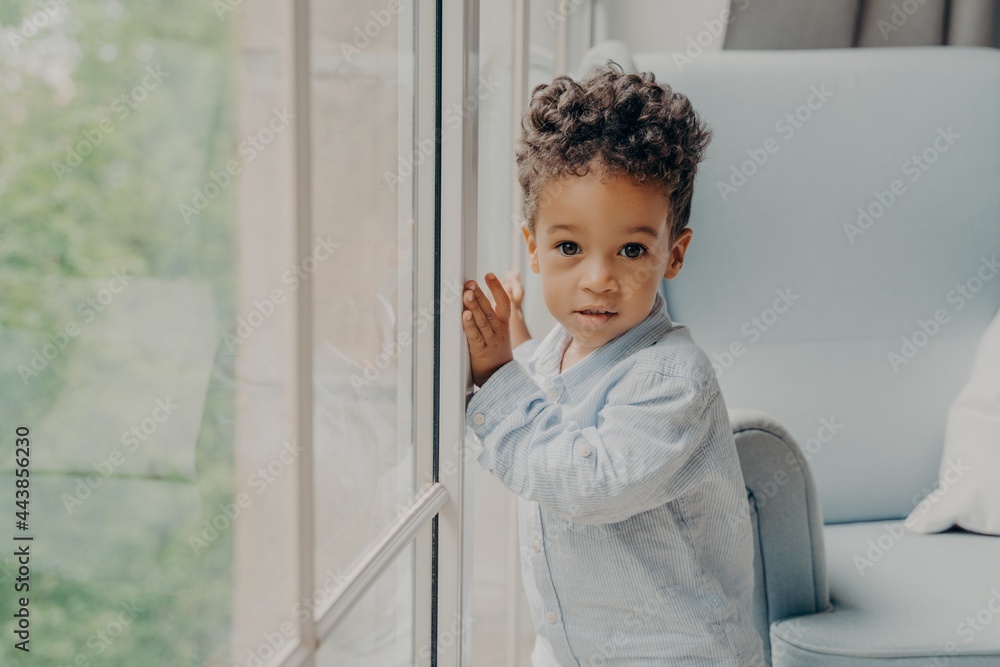 Portrait of cute mixed race curly haired baby boy waiting for parents near window Portrait of cute mixed race curly haired baby boy waiting for parents near window